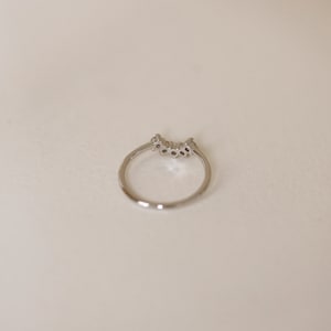 May include: A silver ring with a row of small clear stones set in a curved design.