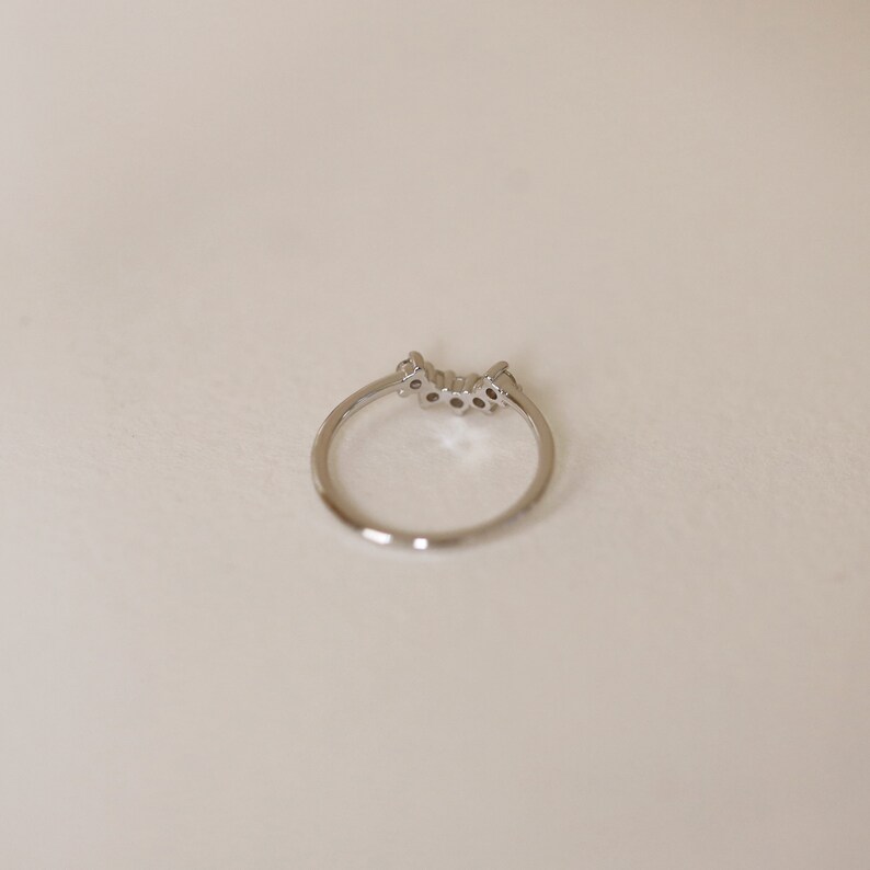 May include: A silver ring with a row of small clear stones set in a curved design.