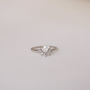 May include: A silver ring with a row of small, clear diamonds set in a crescent shape.