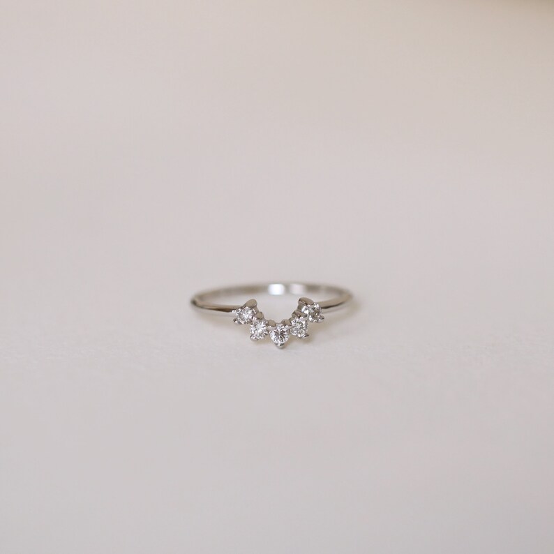 May include: A silver ring with a row of small, clear diamonds set in a crescent shape.