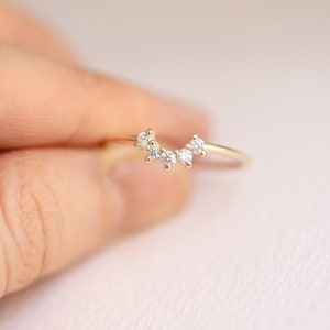May include: A delicate gold ring with a curved row of five small, clear diamonds.