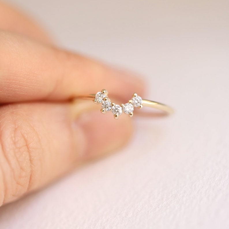 May include: A delicate gold ring with a curved row of five small, clear diamonds.