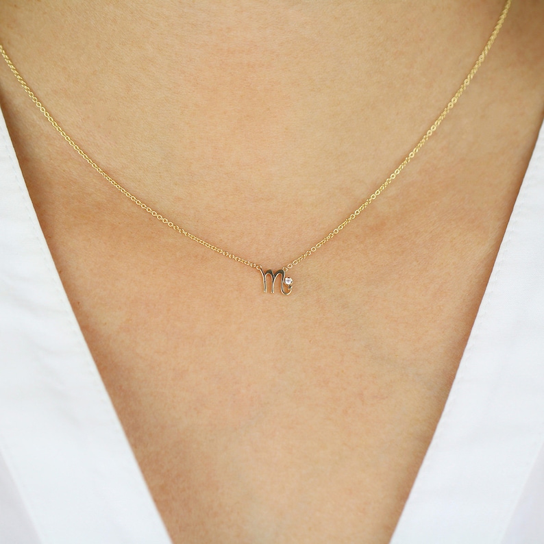 Puede incluir: Un collar de oro con un peque&ntilde;o y delicado colgante en forma del signo astrol&oacute;gico Virgo. El colgante tiene un peque&ntilde;o diamante en el centro.