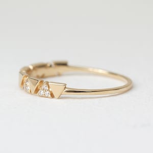 Pu&ograve; includere: Un delicato anello d'oro con una serie di piccole forme triangolari. Ogni triangolo &egrave; adornato da minuscole gemme scintillanti. La fascia dell'anello &egrave; sottile e lucida, creando un design minimalista ed elegante.