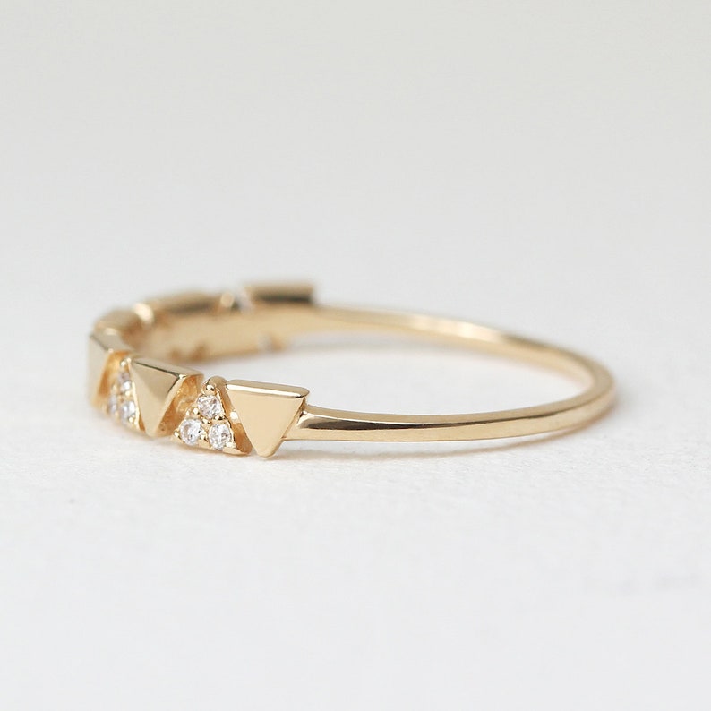 Pu&ograve; includere: Un delicato anello d'oro con una serie di piccole forme triangolari. Ogni triangolo &egrave; adornato da minuscole gemme scintillanti. La fascia dell'anello &egrave; sottile e lucida, creando un design minimalista ed elegante.