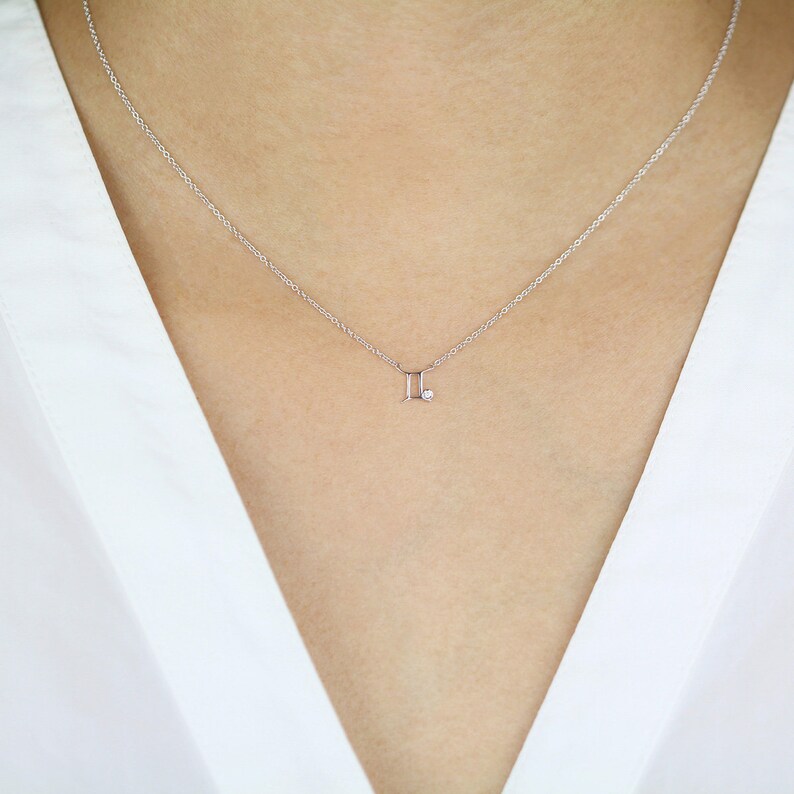 May include: A delicate silver necklace with a Gemini zodiac symbol pendant featuring a small diamond accent.