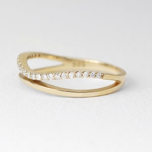 May include: A gold-colored ring with a double-band design. The top band is adorned with small, clear gemstones. The ring is set against a white background, highlighting its elegant and delicate features. A piece of jewelry.