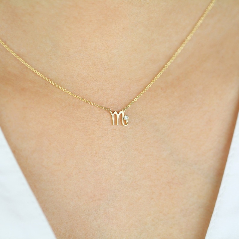 Puede incluir: Un collar de oro con un peque&ntilde;o colgante con el signo del zod&iacute;aco Virgo y un acento de diamante.