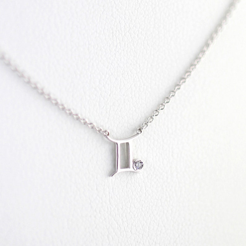 May include: A silver necklace with a Gemini zodiac symbol pendant and a small clear crystal.