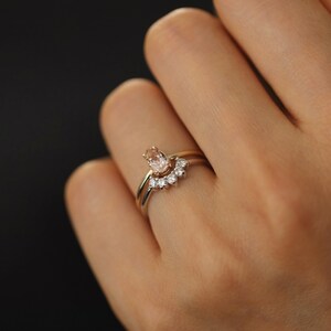 May include: A pair of gold rings with a pear-shaped pink gemstone and a row of smaller diamonds. The rings are worn on a finger.