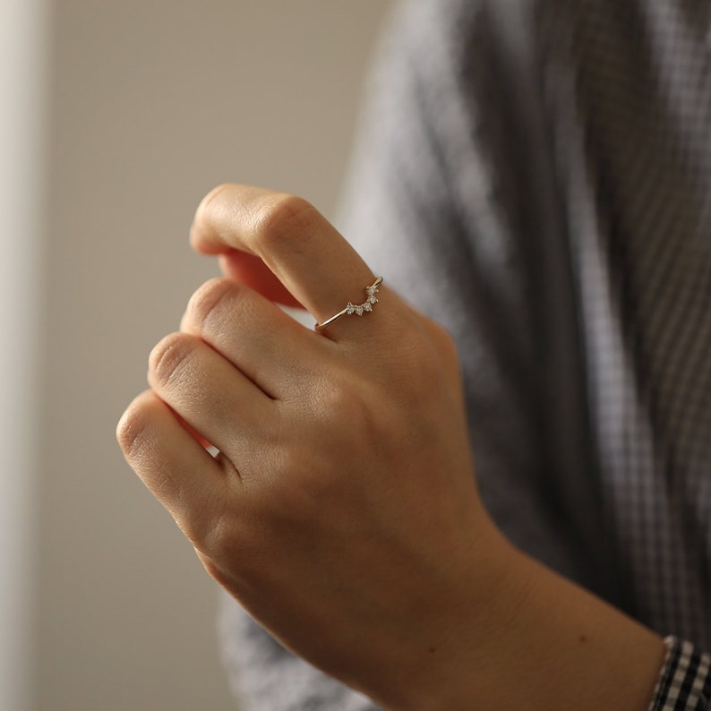May include: A gold ring with a row of small, clear stones set in a curved shape.