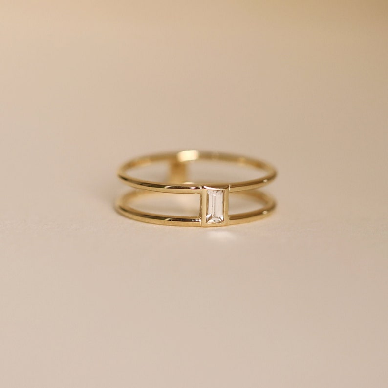 May include: A gold ring with a double band and a single, rectangular, clear stone set in the center.