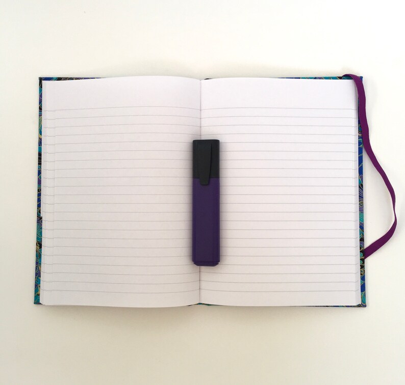 May include: An open notebook with lined pages and a purple highlighter. The notebook has a patterned cover with blue, green, and gold accents. A purple ribbon bookmark is attached to the spine.
