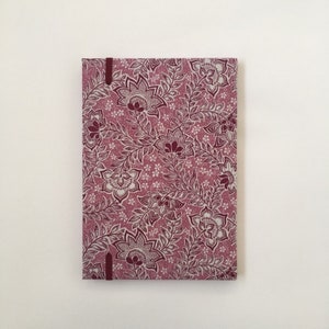 May include: A rectangular notebook with a floral pattern in shades of burgundy and white. The cover features a repeating design of stylized flowers and leaves. A burgundy ribbon bookmark is visible.