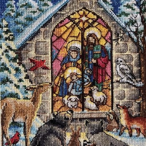 Könnte beinhalten: Ein Kreuzstich-Darstellung einer winterlichen Weihnachtskrippe. Das Bild zeigt eine Kirche mit einem Buntglasfenster, das Maria, Josef und das Jesuskind darstellt. Tiere und Vögel, darunter Hirsche, Füchse und Eulen, umgeben die Kirche in einer verschneiten Landschaft.