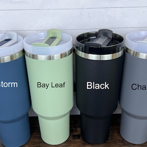 Op de afbeelding: Vier roestvrijstalen reistassen met verschillende poedercoatings. De bekers zijn gelabeld met "Storm", "Bay Leaf", "Black" en "Charcoal".