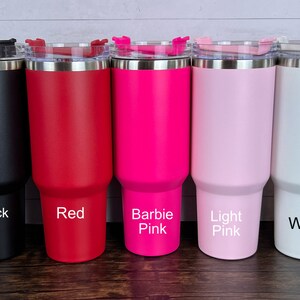 Op de afbeelding: Vijf roestvrijstalen bekers met deksels in verschillende kleuren: zwart, rood, felroze, lichtroze en wit. De bekers zijn gelabeld met hun kleuren.