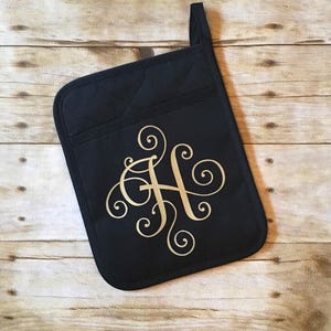May include: Black oven mitt with a gold monogram of the letter "H" in a decorative script font.
