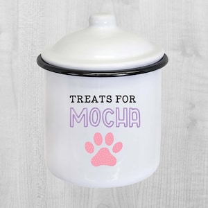 May include: White enamel treat jar with a black rim and lid. The jar has a pink paw print with white polka dots and the text "Treats for Mocha" in purple.