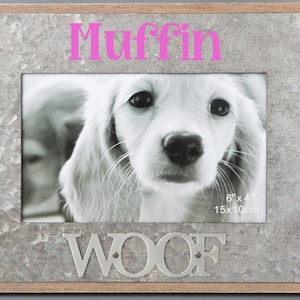 May include: A silver metal picture frame with a wood border. The frame has a 6x4 inch photo opening and the word "WOOF" is embossed on the bottom. The name "Muffin" is written in pink letters at the top of the frame.