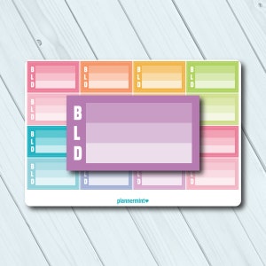 May include: A sheet of planner stickers with a variety of colorful rectangular designs. Each rectangle features a gradient of colors, with the letters "BLD" printed vertically on the left side. A larger, lavender rectangle is centered, also with "BLD" and a gradient.