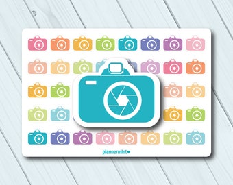 Può includere: Un foglio di adesivi colorati a forma di macchina fotografica in varie tonalità, tra cui blu, arancione, verde e viola. Un grande adesivo a forma di macchina fotografica turchese è in evidenza, con il testo "plannermint" in basso.