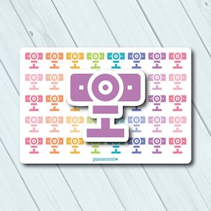 May include: A sheet of planner stickers featuring a repeating pattern of colorful webcam icons. A larger, purple webcam sticker is centered on the sheet. The stickers are in shades of pink, orange, yellow, green, blue, and purple.