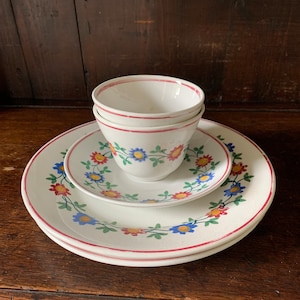May include: A set of three white ceramic teacups with a floral design in red, yellow, blue, and green. The cups are stacked on top of each other and are sitting on a white saucer with a matching floral design.