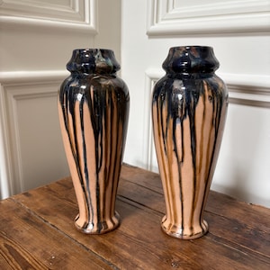 Pode incluir: Dois vasos de cerâmica com base castanha clara e esmalte gotejado azul escuro. Os vasos têm uma base alargada e um topo ligeiramente mais largo. São exibidos numa superfície de madeira.