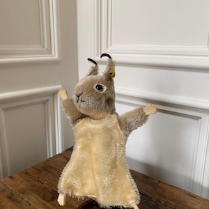Puede incluir: Un títere de ardilla Steiff vintage con un cuerpo de piel beige y una cara de fieltro marrón. El títere lleva un vestido de fieltro beige y tiene una base de madera.