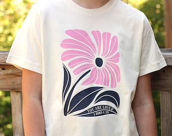 You Are Loved Christian Shirt for Girls and Tweens on a youth fit shirt style with a cute Faith-Based Flower and 1 John 4:19 Bible Verse