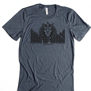 May include: A dark blue t-shirt with a black graphic of a lion wearing a crown and the text "King of Kings" with the words "Dedicated to His" below.