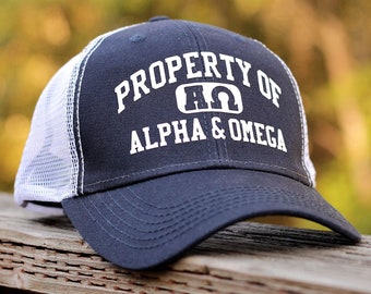 May include: A navy blue and white trucker hat with the text "PROPERTY OF ALPHA & OMEGA" and a white Greek letter symbol.
