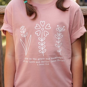 May include: A pink t-shirt with a white floral design and the text "grow in the grace and knowledge of our Lord and Savior Jesus Christ 2 Peter 3:18".