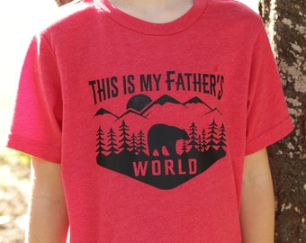 May include: Red t-shirt with a black graphic design that says "This is my father's world" with a bear and mountains.