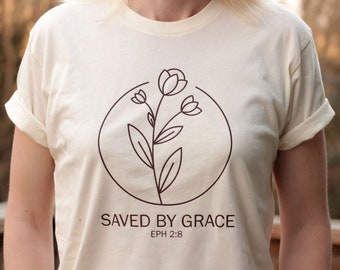 May include: A cream-colored t-shirt with a brown floral design and the text "SAVED BY GRACE EPH 2:8".