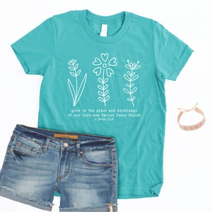 May include: Teal blue t-shirt with a white floral design and the text "grow in the grace and knowledge of our Lord and Savior Jesus Christ 2 Peter 3:10".
