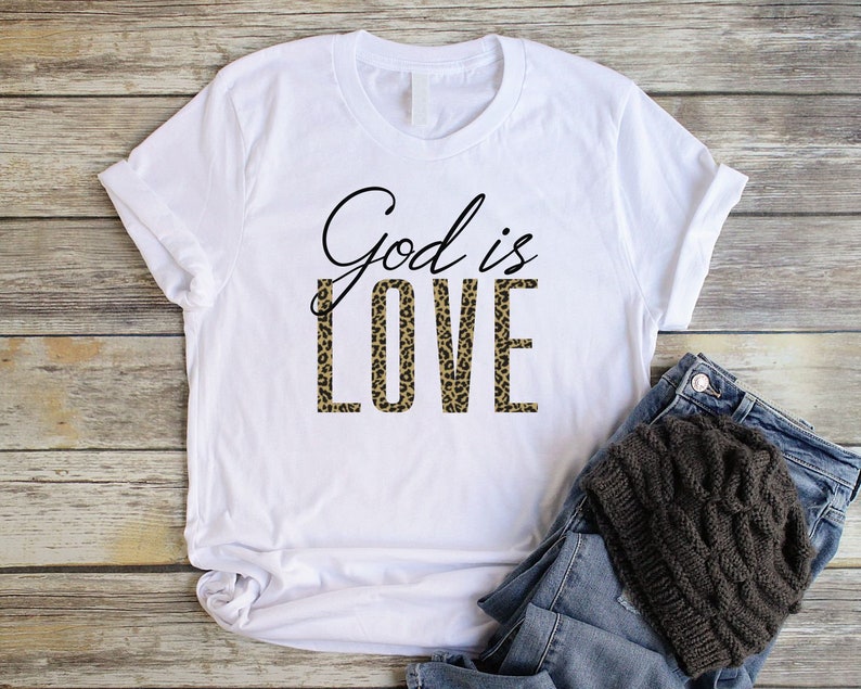 May include: White t-shirt with the text "God is Love" printed in black. The word "Love" is printed in a leopard print pattern.