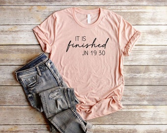 May include: A light pink t-shirt with the text "IT IS finished JN 19 30" printed in black.