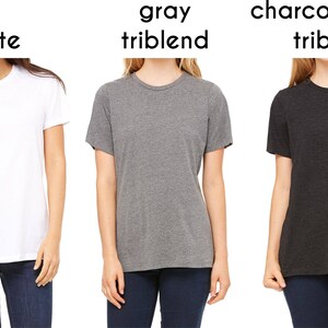 May include: Three t-shirts in different colors: white, gray triblend, and charcoal black triblend. The shirts are all crew neck and short-sleeved.