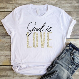 May include: White t-shirt with the text "God is Love" printed in black. The word "Love" is printed in a leopard print pattern.