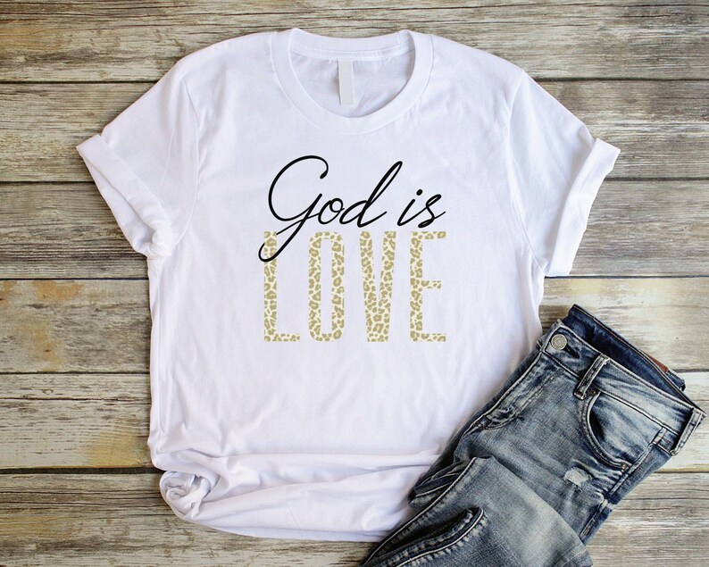 May include: White t-shirt with the text "God is Love" printed in black. The word "Love" is printed in a leopard print pattern.