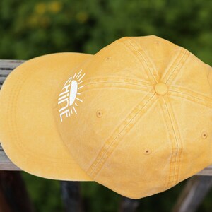 May include: A yellow baseball cap with a white sun and the word "shine" embroidered on the front.