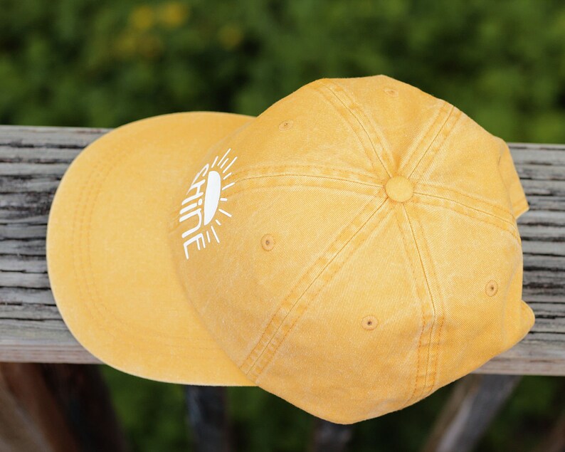 May include: A yellow baseball cap with a white sun and the word "shine" embroidered on the front.