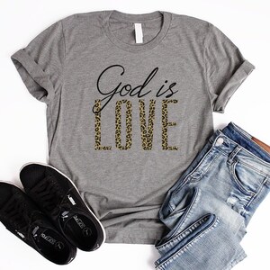 May include: A gray t-shirt with the text "God is Love" printed on it. The word "Love" is in a leopard print pattern.