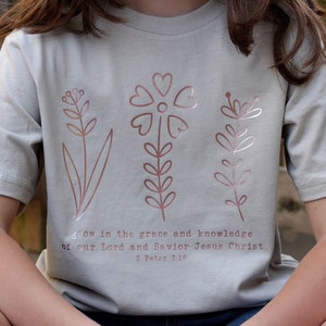 May include: A light gray t-shirt with a rose gold floral design and the text "grow in the grace and knowledge of our Lord and Savior Jesus Christ 2 Peter 3:18".