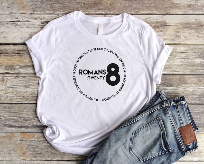 May include: White t-shirt with a black circle graphic featuring the text "Romans : Twenty Eight" and the number "8" in a larger font.