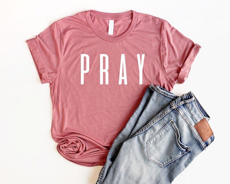 May include: A dusty rose colored t-shirt with the word "PRAY" printed in white on the front.