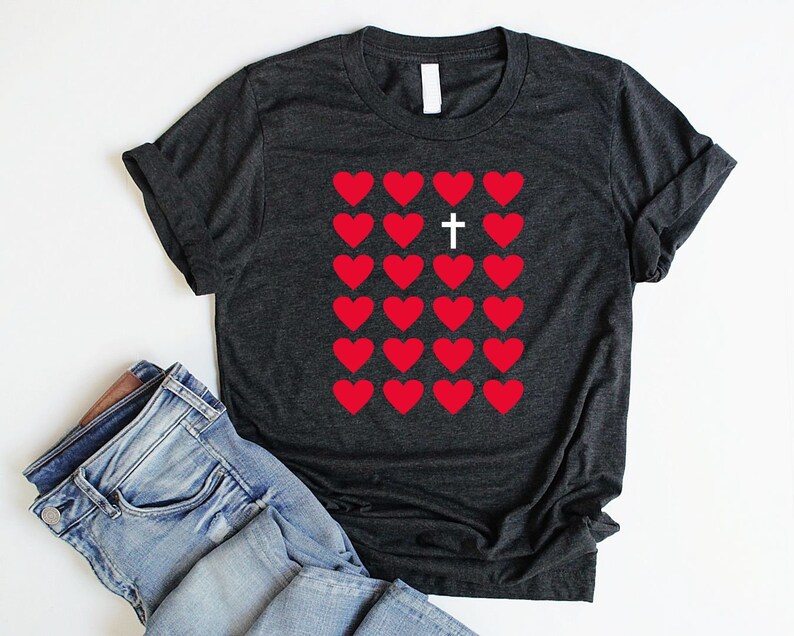 May include: A dark gray t-shirt with a graphic of red hearts and a white cross in the center. The cross is surrounded by hearts.