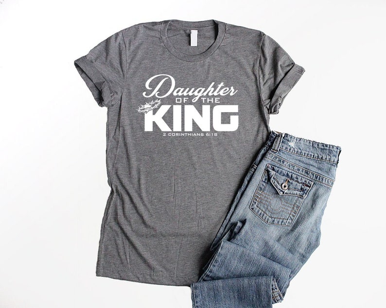 Op de afbeelding: Grijs T-shirt met witte tekst die "Daughter of the King" en "2 Corinthians 6:18" zegt.
